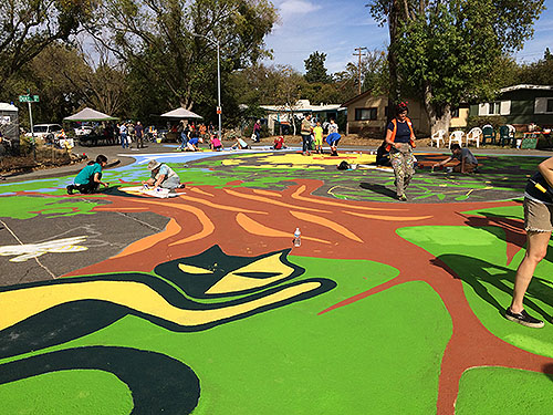 Danielle Fodor (walking on the right), the artist who designed the street mural, helps community volunteers with creating a beautiful mural.